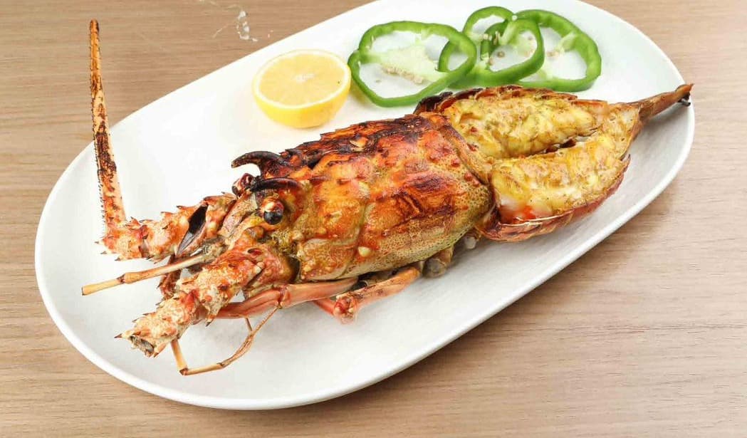 Whole grilled lobster on a white platter with lemon and green pepper