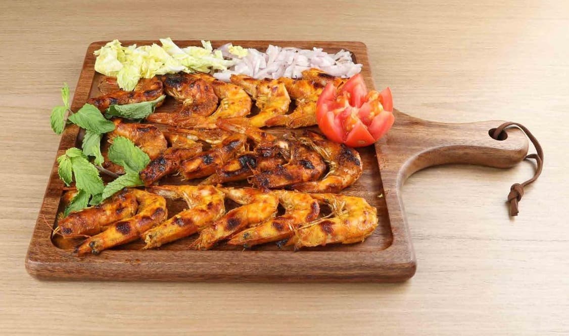 Grilled prawns on a wooden board with mint, onion and tomato