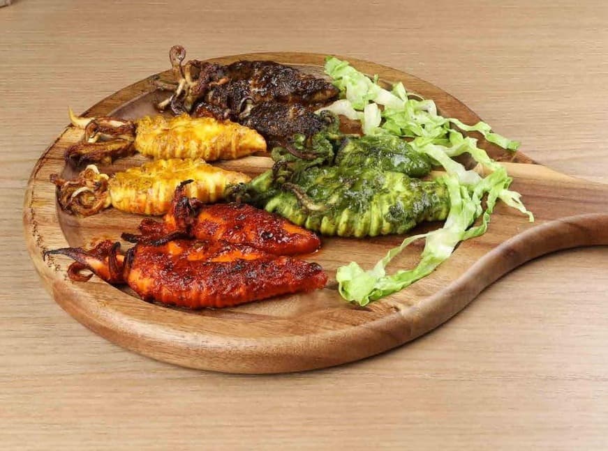Grilled squid in red, yellow, green and black marinades on a round wooden board