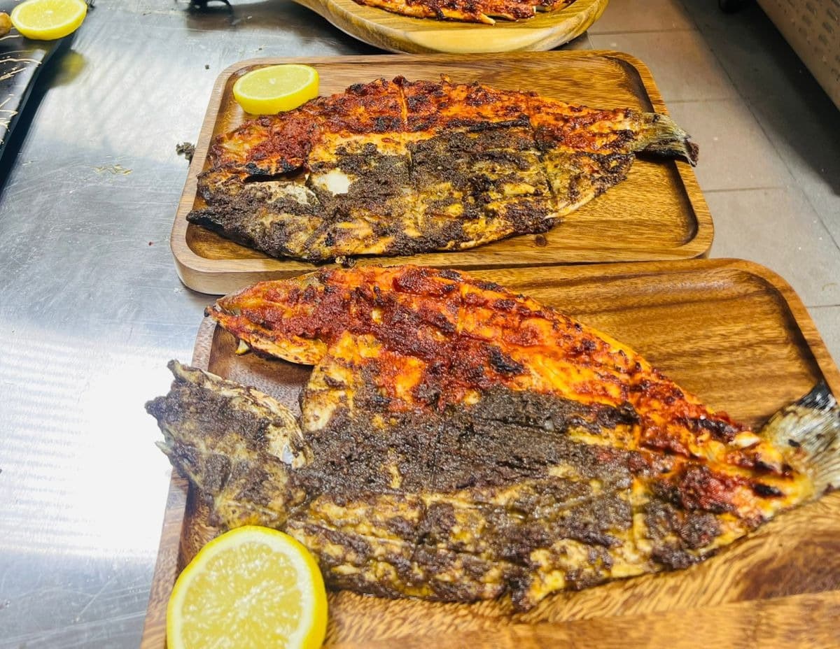 Butterflied whole fish grilled in red and black marinades on wooden boards