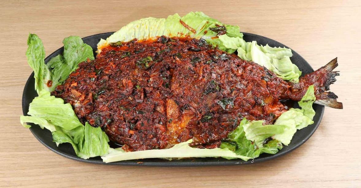 Whole grilled fish coated in red masala on a black platter with lettuce