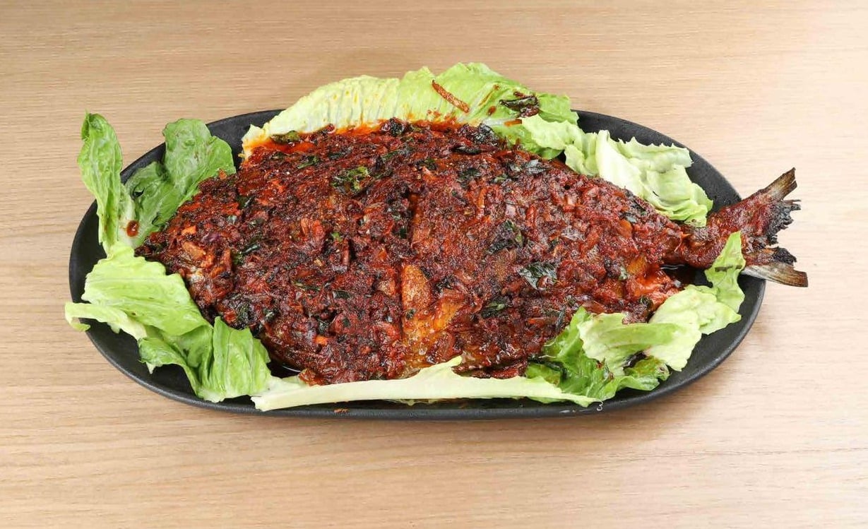 Whole grilled fish coated in red masala on a black platter with lettuce