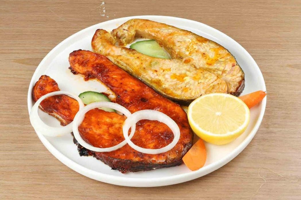 Two salmon steaks in red and yellow marinades with onion rings and lemon